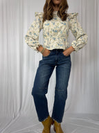 Person wearing a floral blouse, blue jeans, and yellow boots against a white background