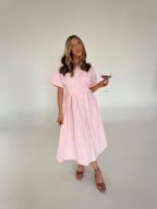 Woman in a pink and white striped dress holding a glass of red wine against a plain background