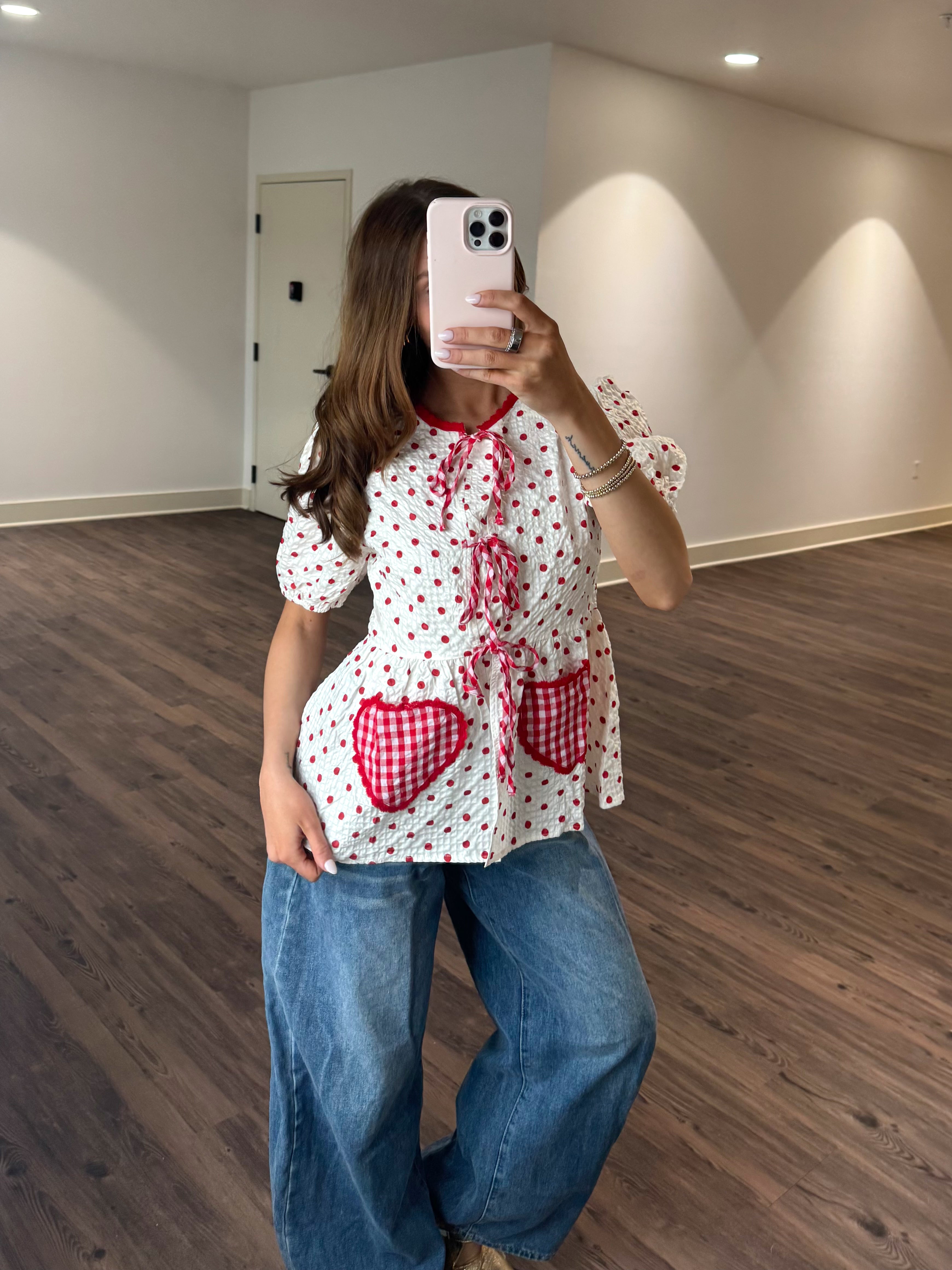 Person wearing a white blouse with red heart patterns and blue jeans in an indoor setting.