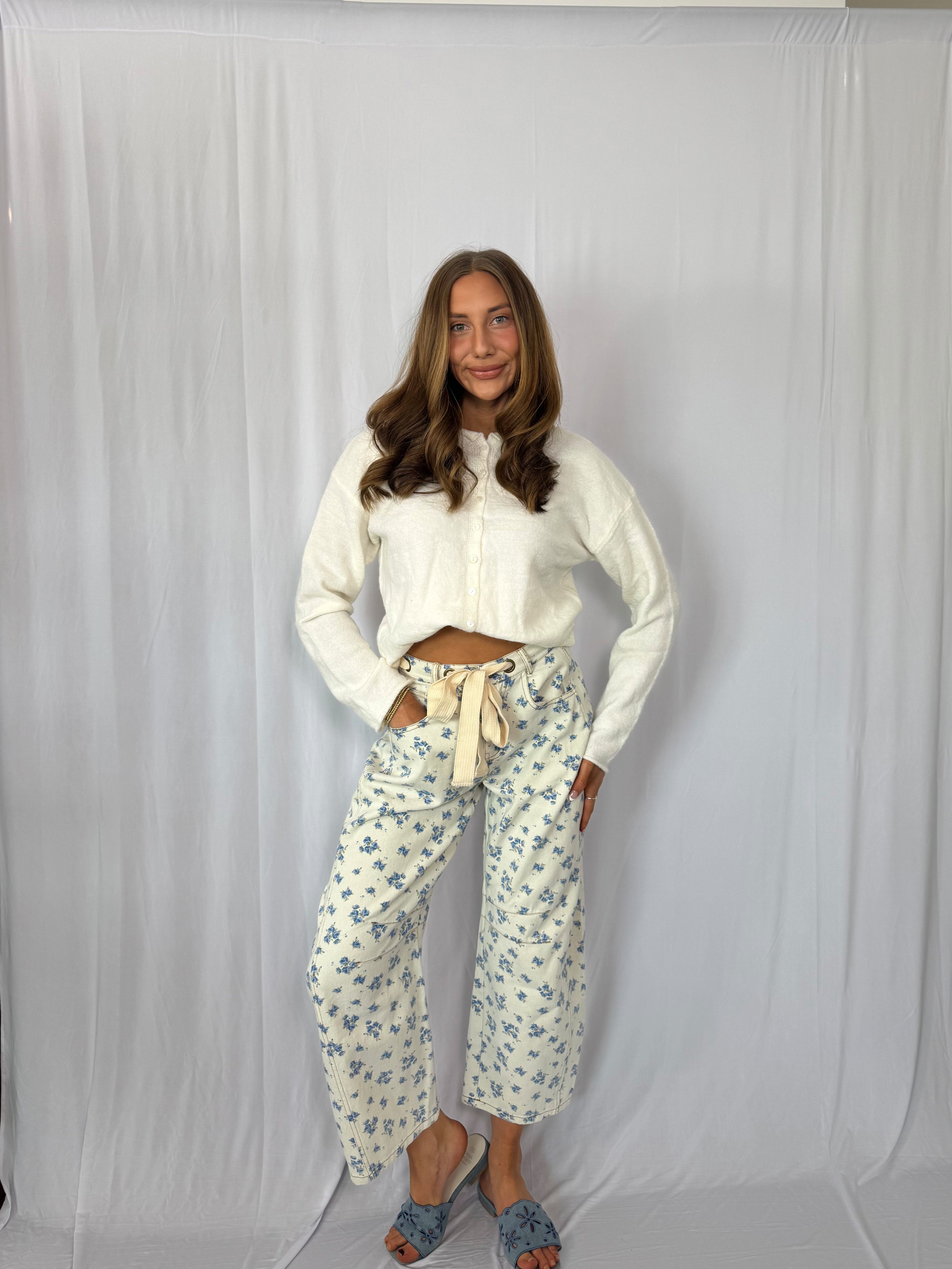 Woman wearing a white blouse and floral pants against a plain background