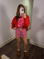 Person wearing a red sweatshirt with text and pink checkered shorts in a room.