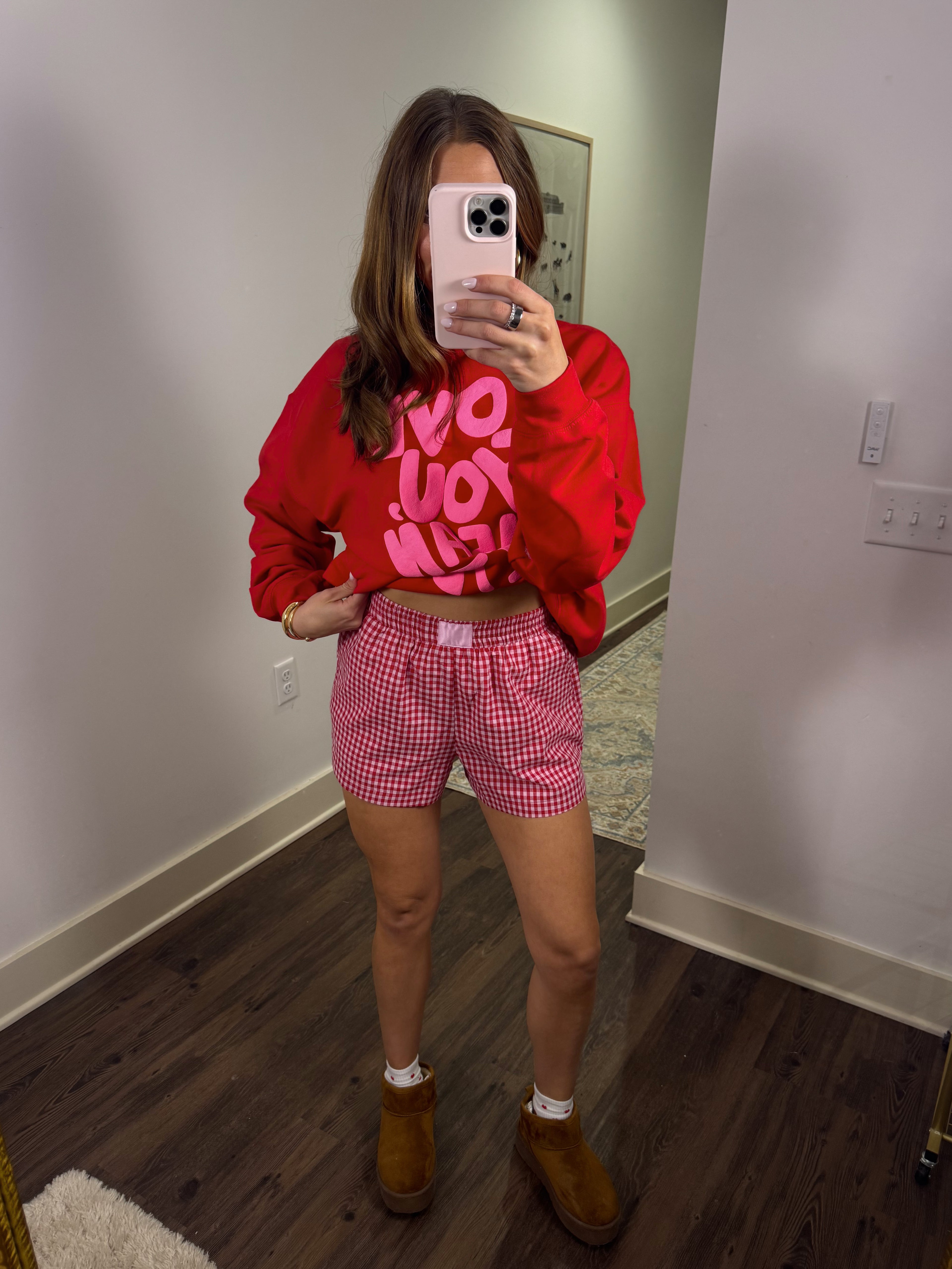 Person wearing a red sweatshirt with text and pink checkered shorts in a room.