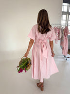 Woman in a pink striped dress holding flowers in a room with clothing racks.