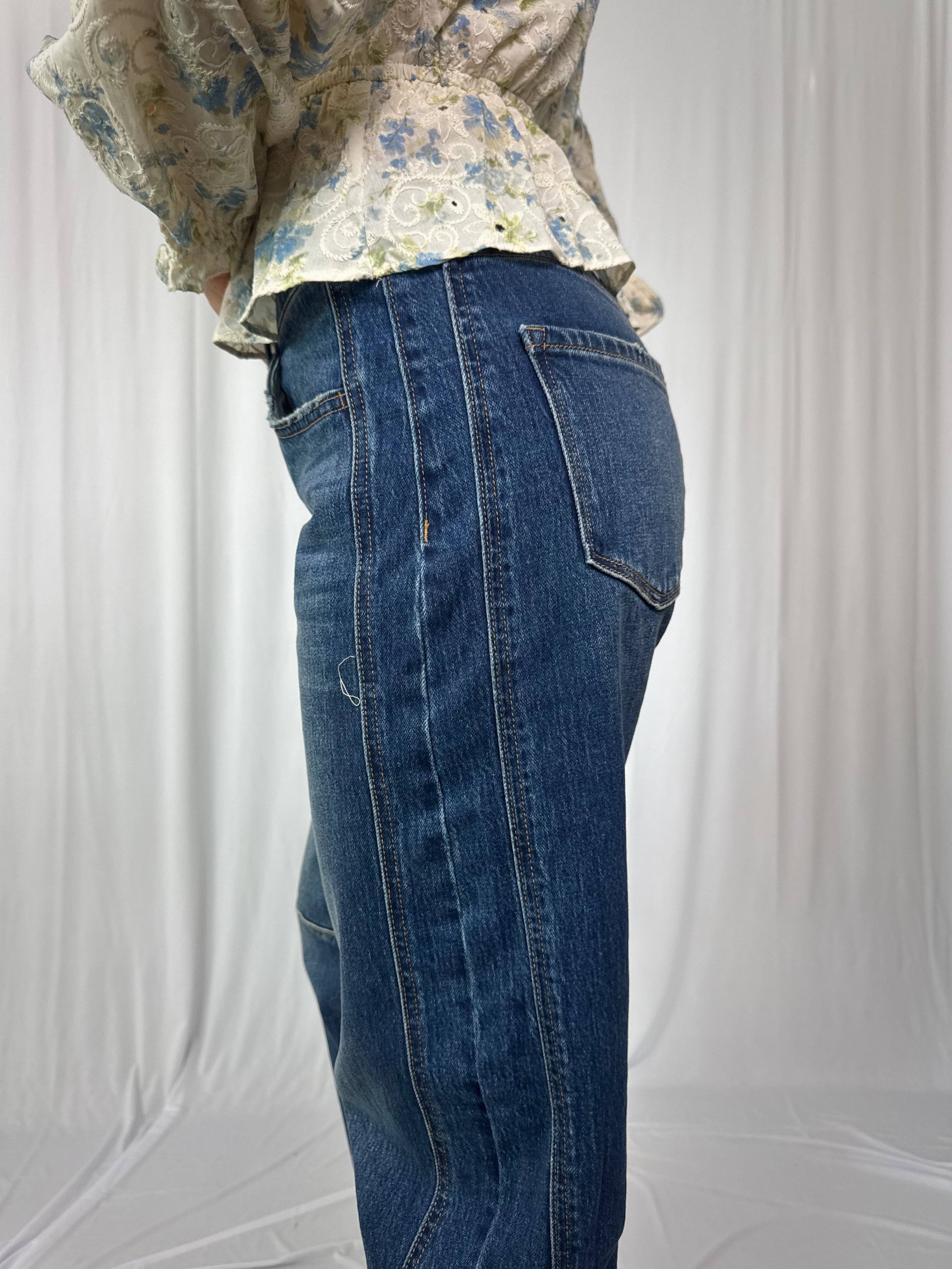 Person wearing blue jeans and a floral top against a white background