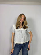 Woman wearing a white blouse with ruffled details and blue jeans against a plain background