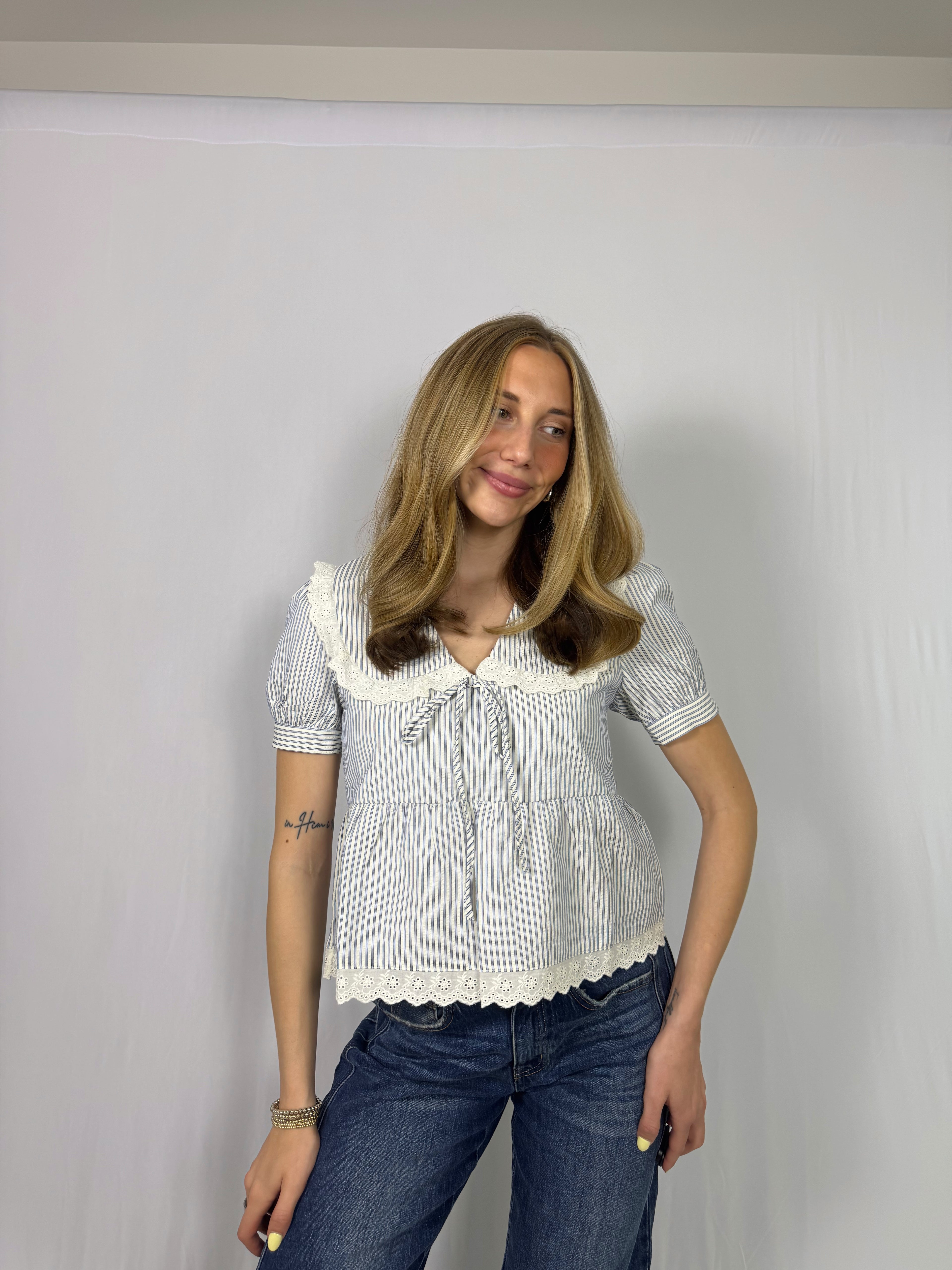 Woman wearing a white blouse with ruffled details and blue jeans against a plain background