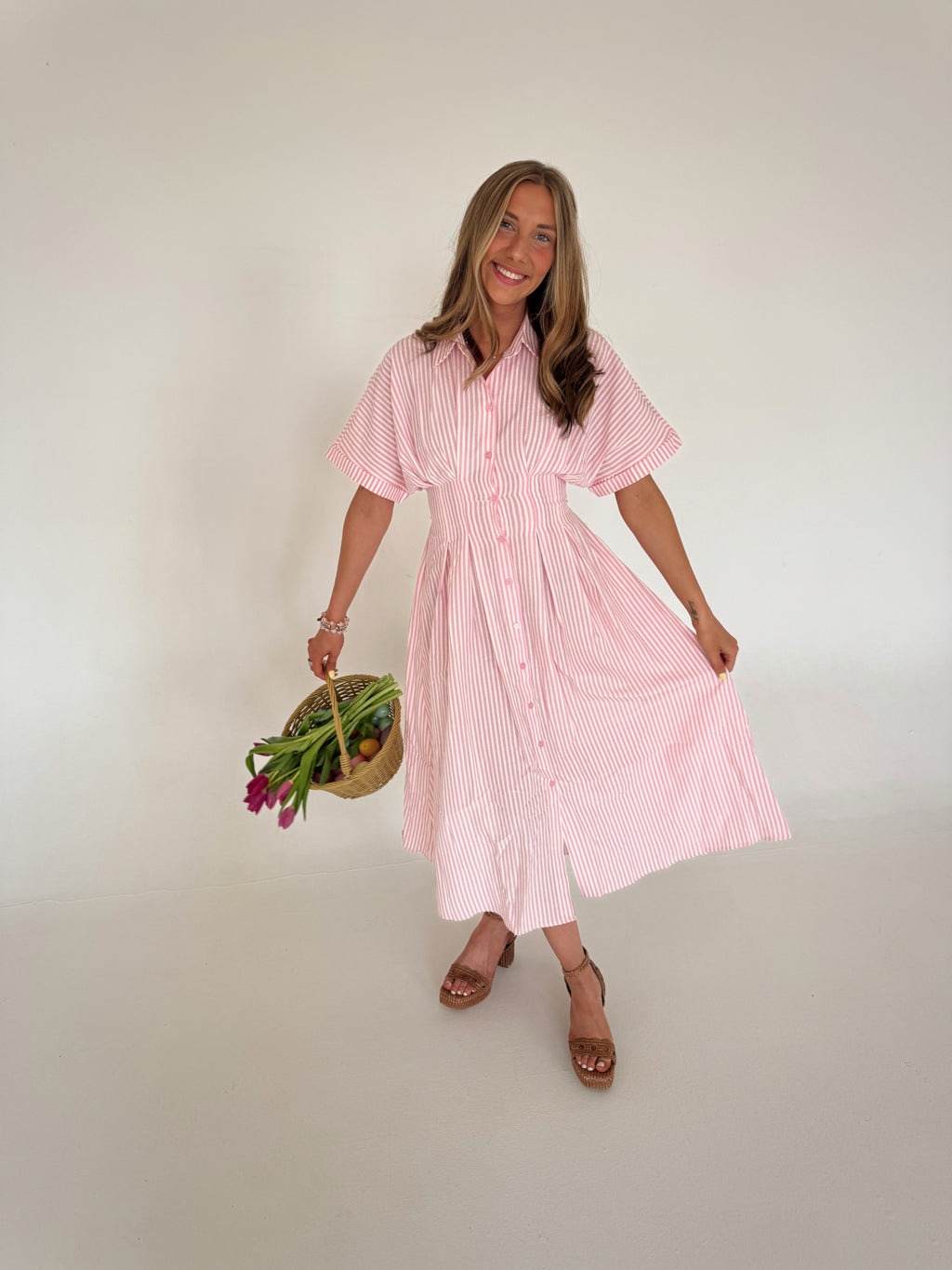 Woman wearing a pink and white striped dress holding tulips against a plain background