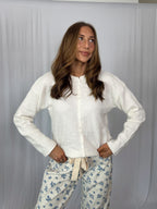 Woman wearing a white blouse and floral pants against a plain background