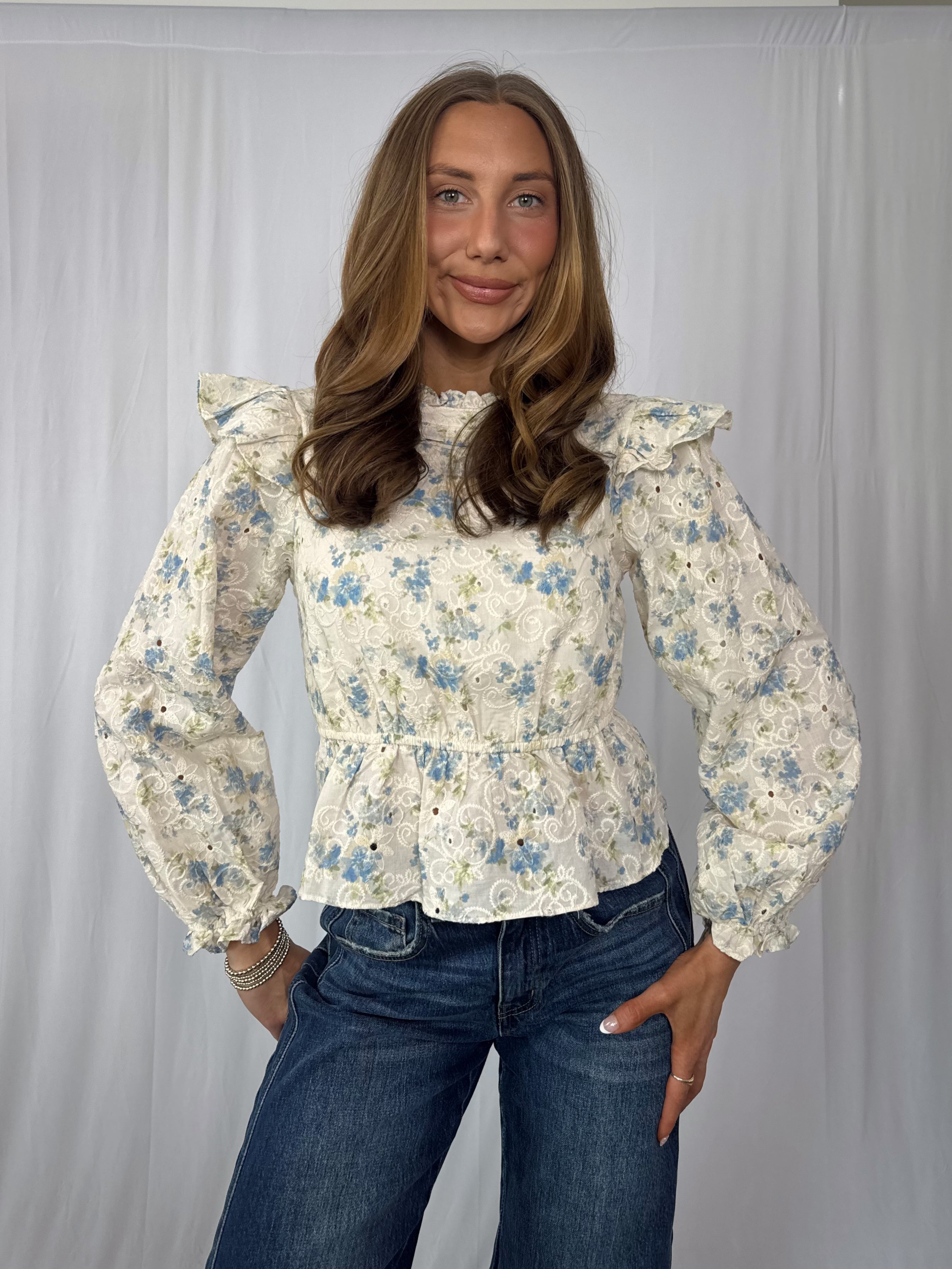 Woman wearing a floral blouse with ruffled sleeves against a plain background
