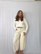 Woman wearing a white cropped jacket and patterned pants against a plain background