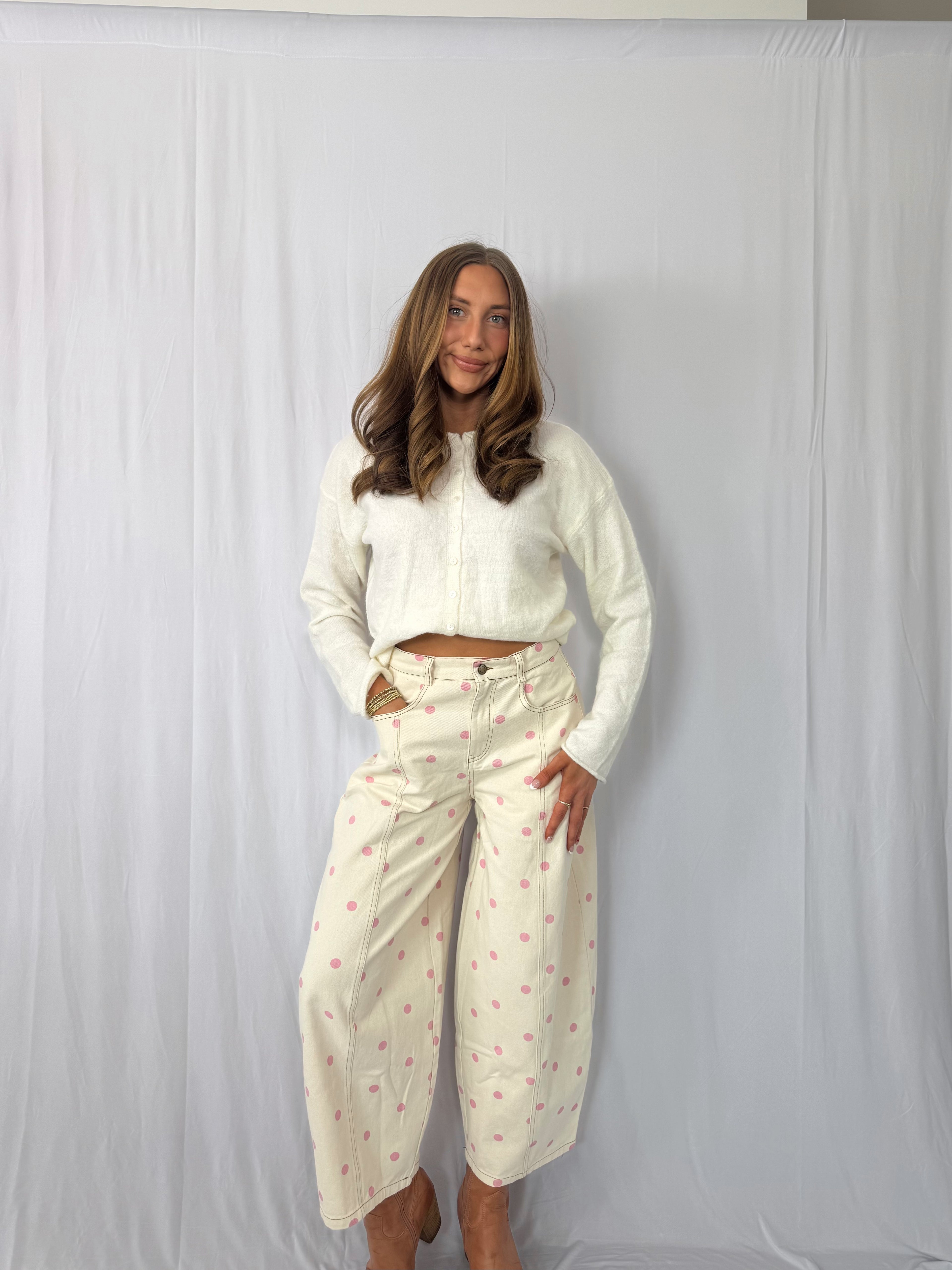 Woman wearing a white cropped jacket and patterned pants against a plain background