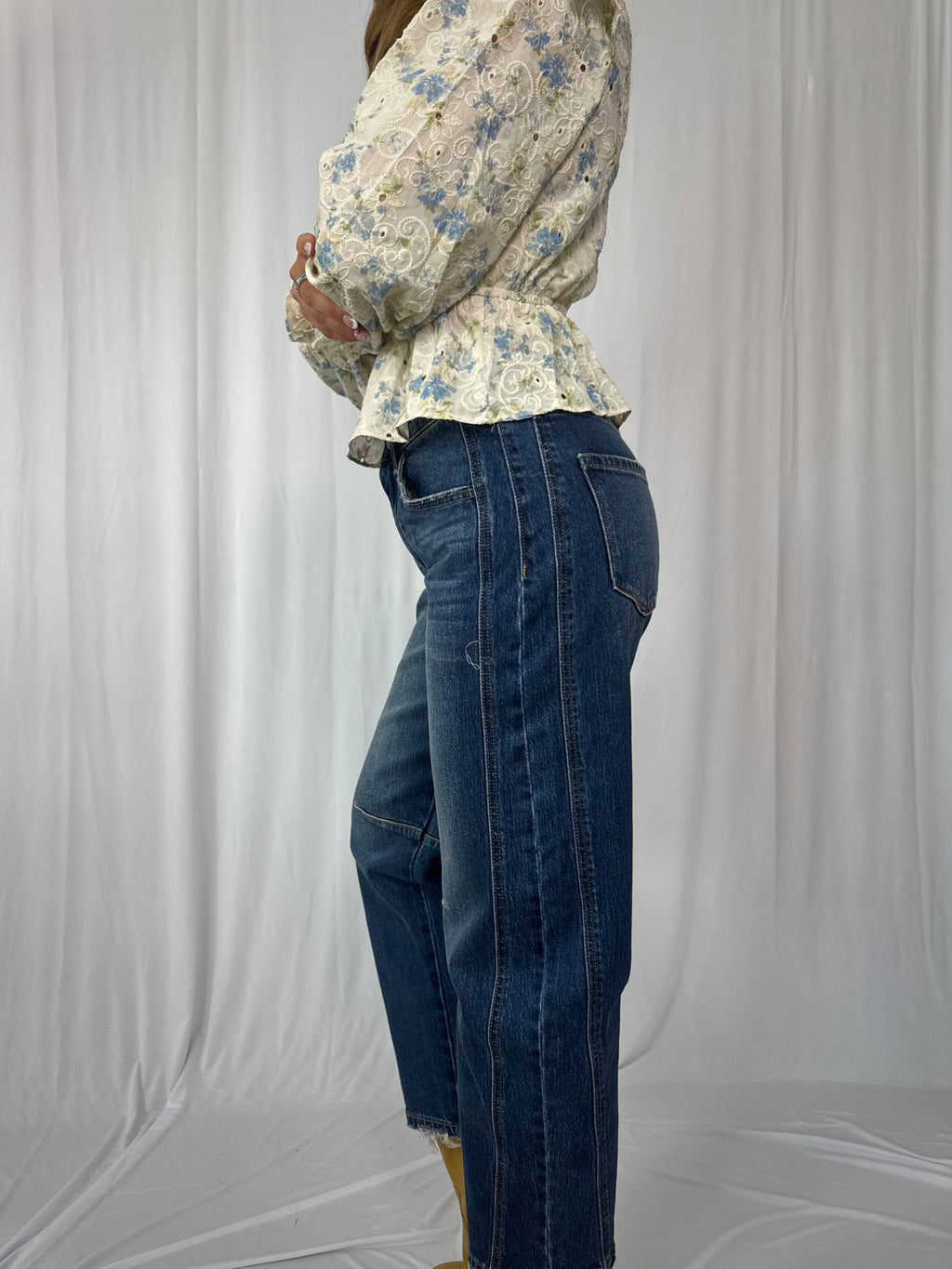 Person wearing a floral blouse and blue jeans against a plain background