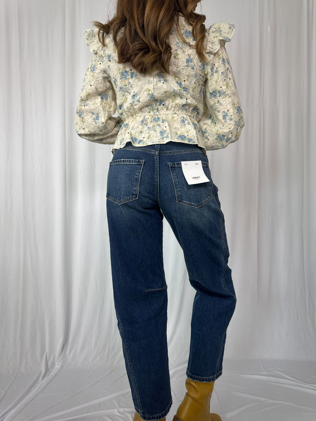 Person wearing a floral blouse and blue jeans on a plain background