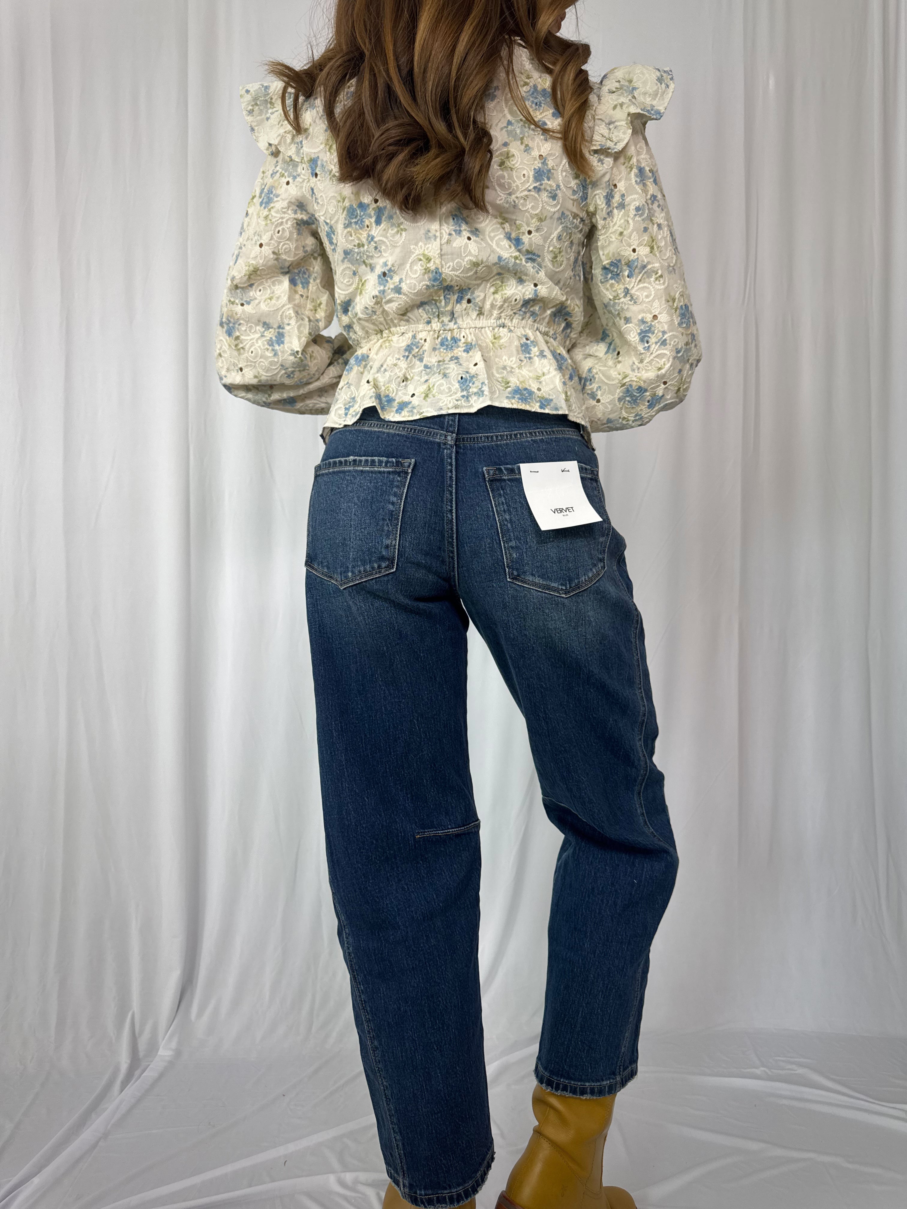 Person wearing a floral blouse and blue jeans on a plain background