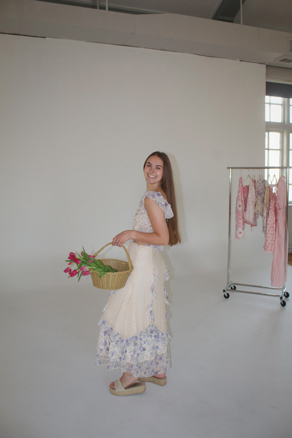 Woman holding a basket with flowers in a minimalistic room.