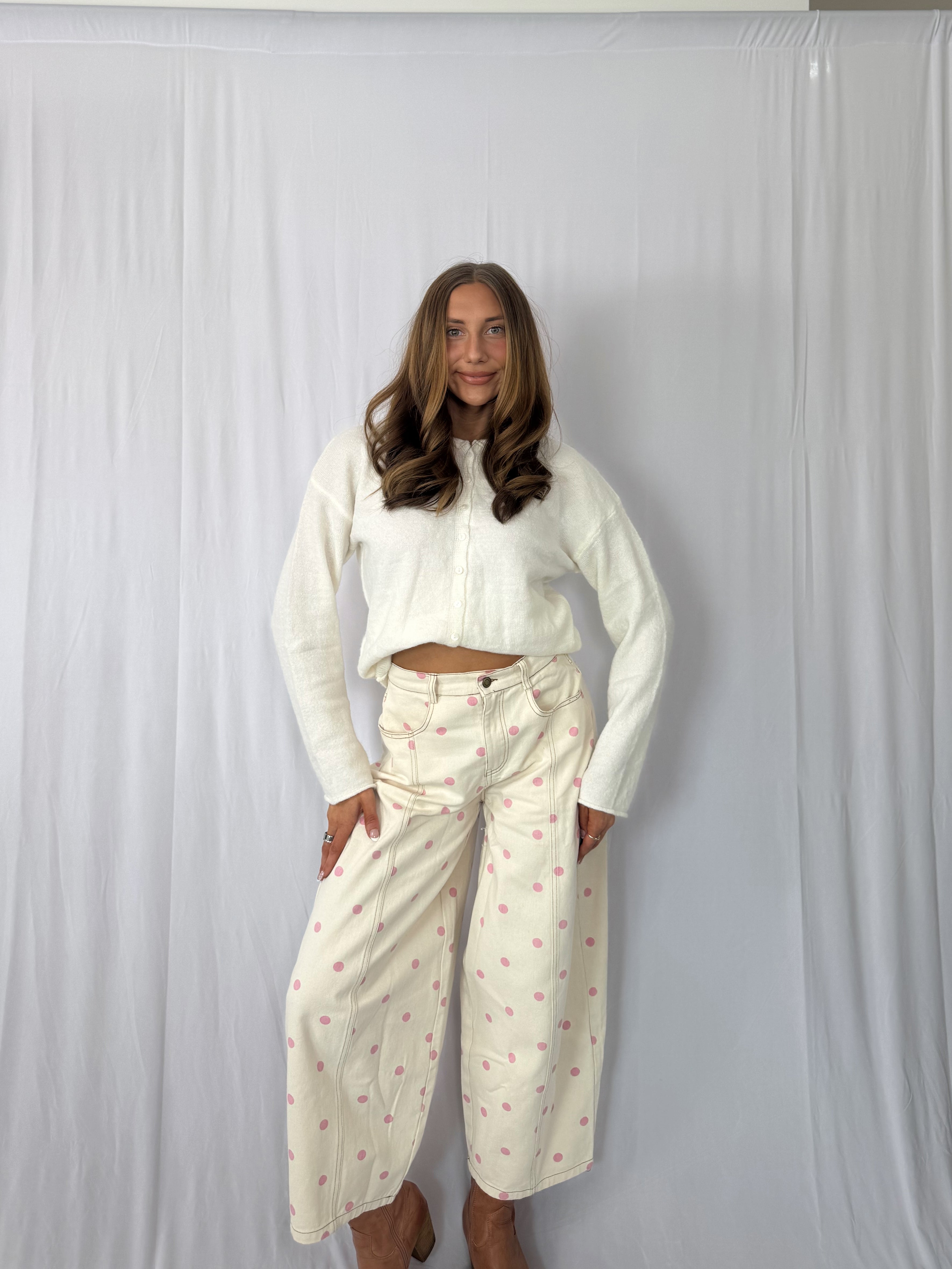 Woman wearing a white long-sleeve top and light-colored pants with a subtle pattern against a plain background