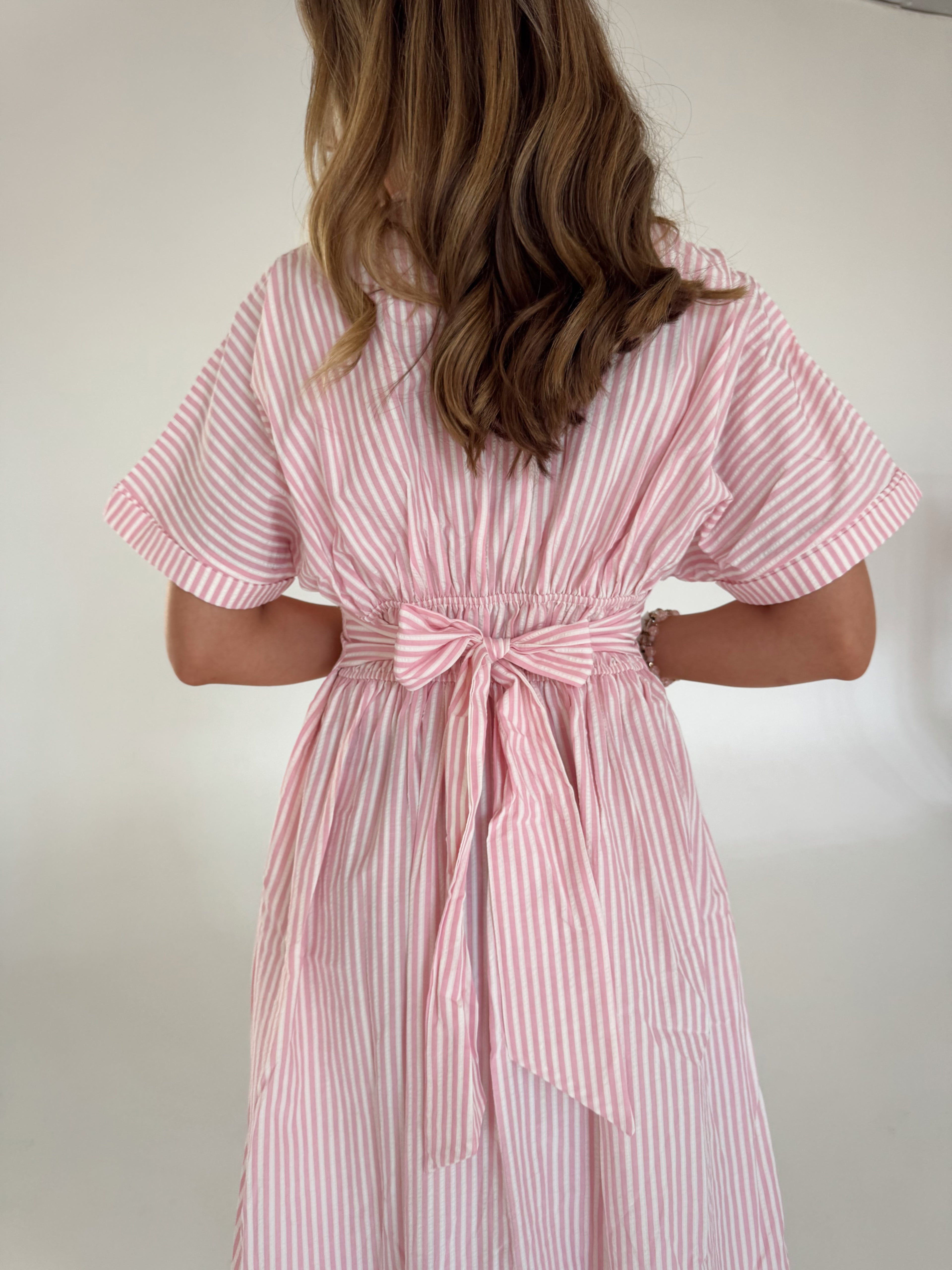 Person wearing a pink and white striped dress with a bow detail on a plain background