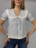Woman wearing a striped blouse with lace details on a plain background