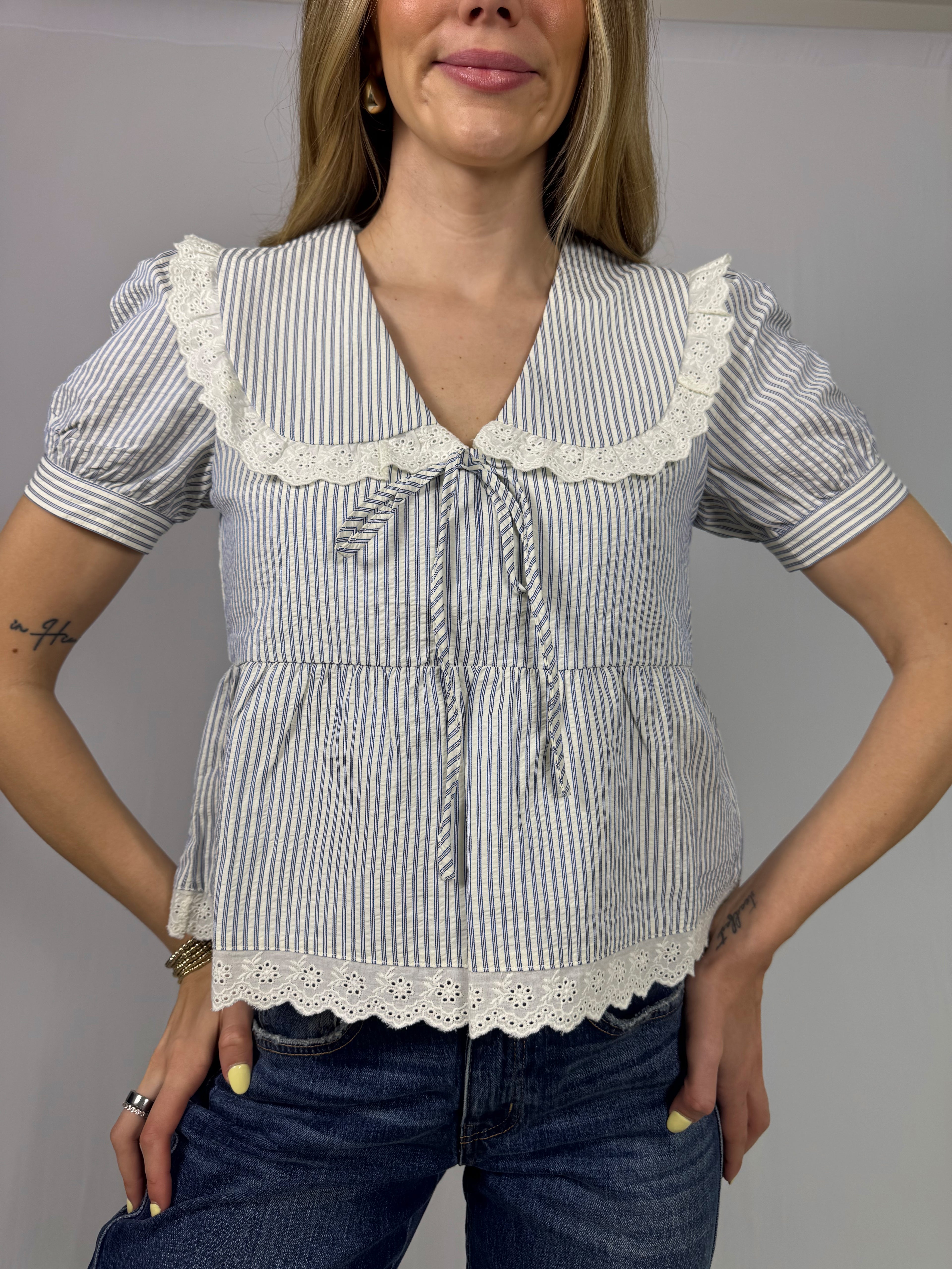 Woman wearing a striped blouse with lace details on a plain background