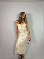 Woman wearing a cream-colored skirt and top with a floral pattern against a plain background