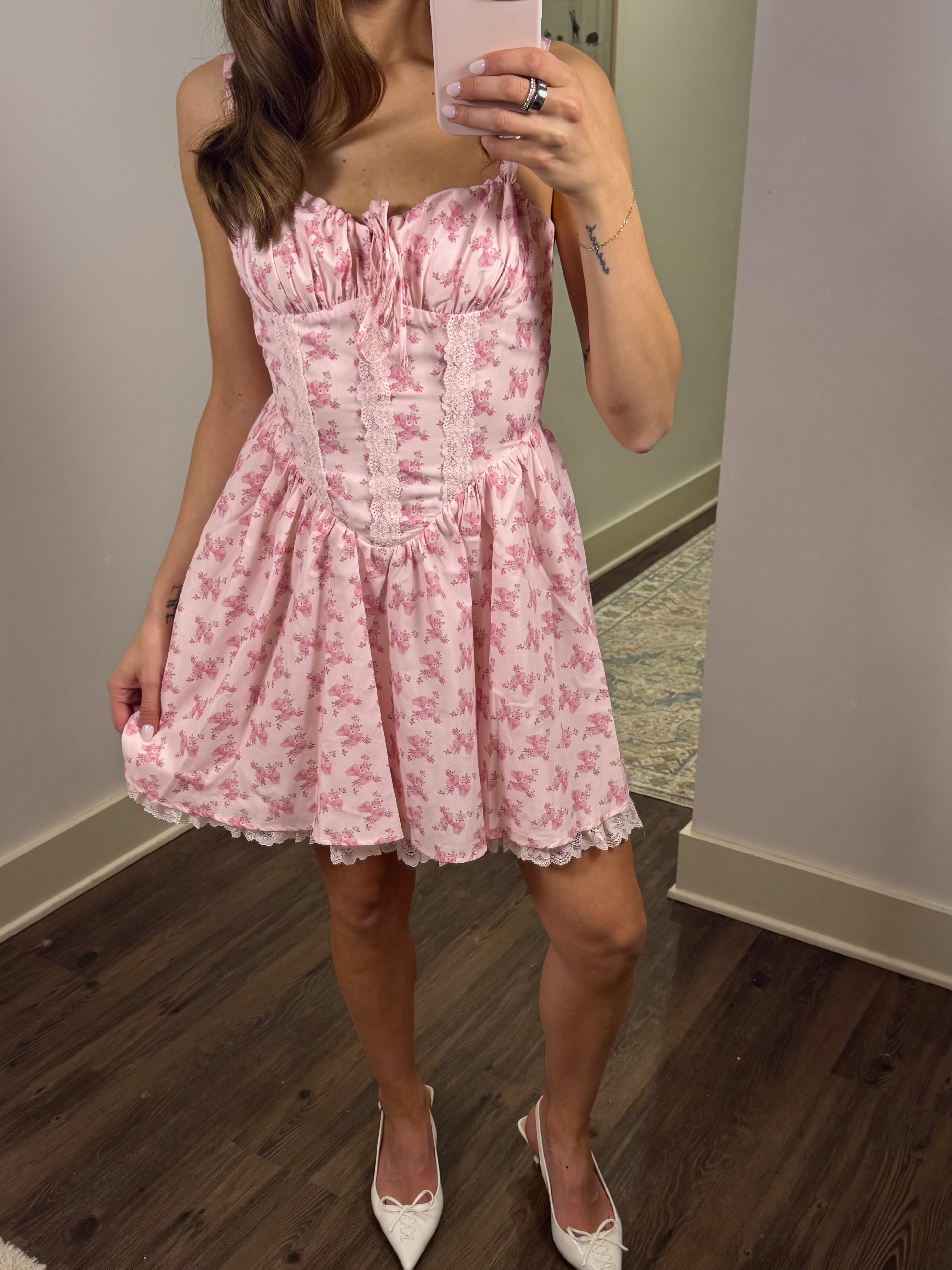 Person wearing a pink floral dress in a room with wooden floor and white walls.
