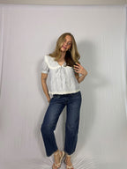 Woman wearing a striped blouse with lace details and dark blue jeans against a white backdrop