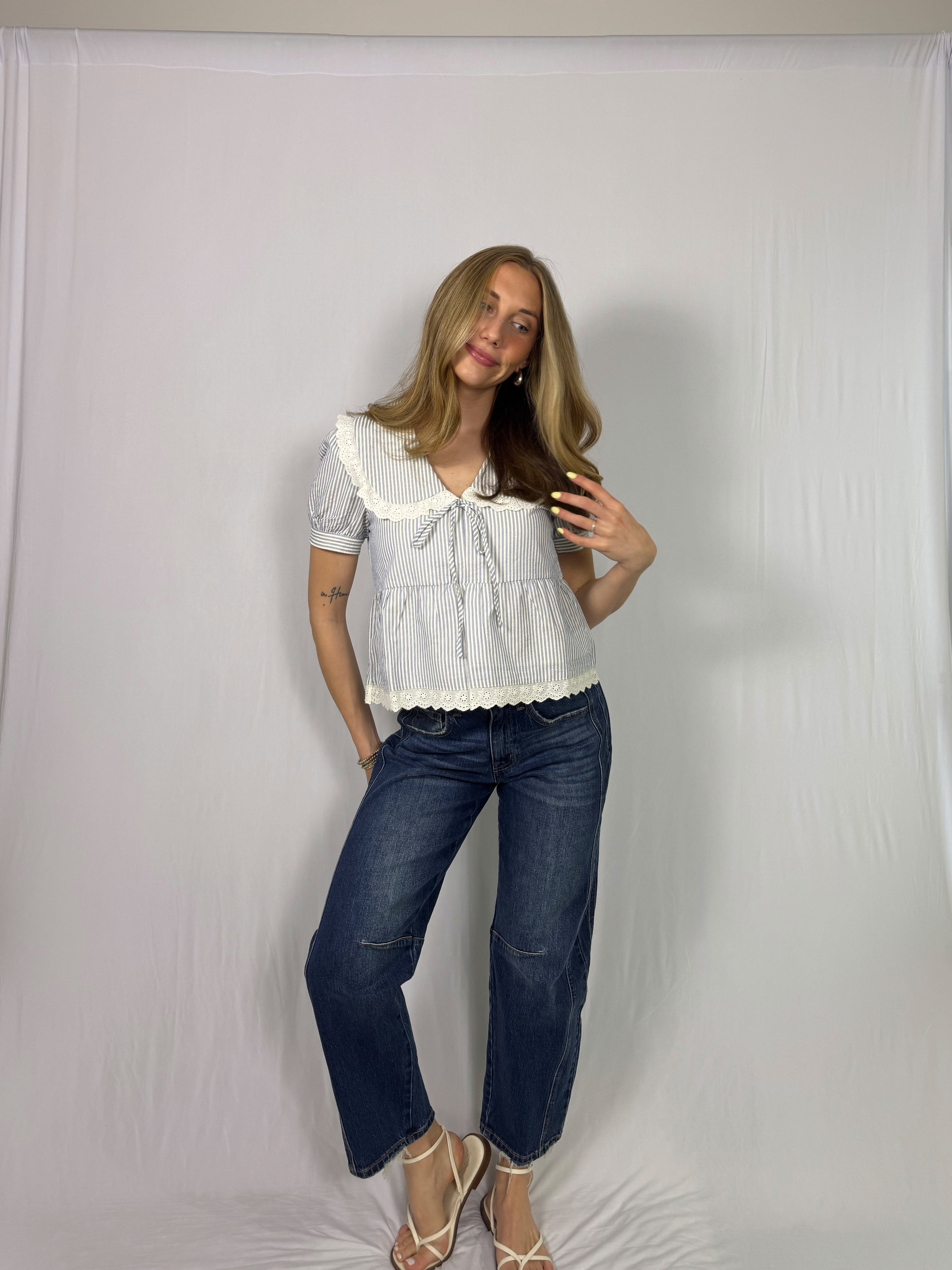 Woman wearing a striped blouse with lace details and dark blue jeans against a white backdrop