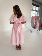 Woman wearing a pink and white striped dress in a minimalistic room.