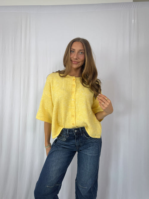 Woman wearing a yellow sweater and blue jeans against a white background