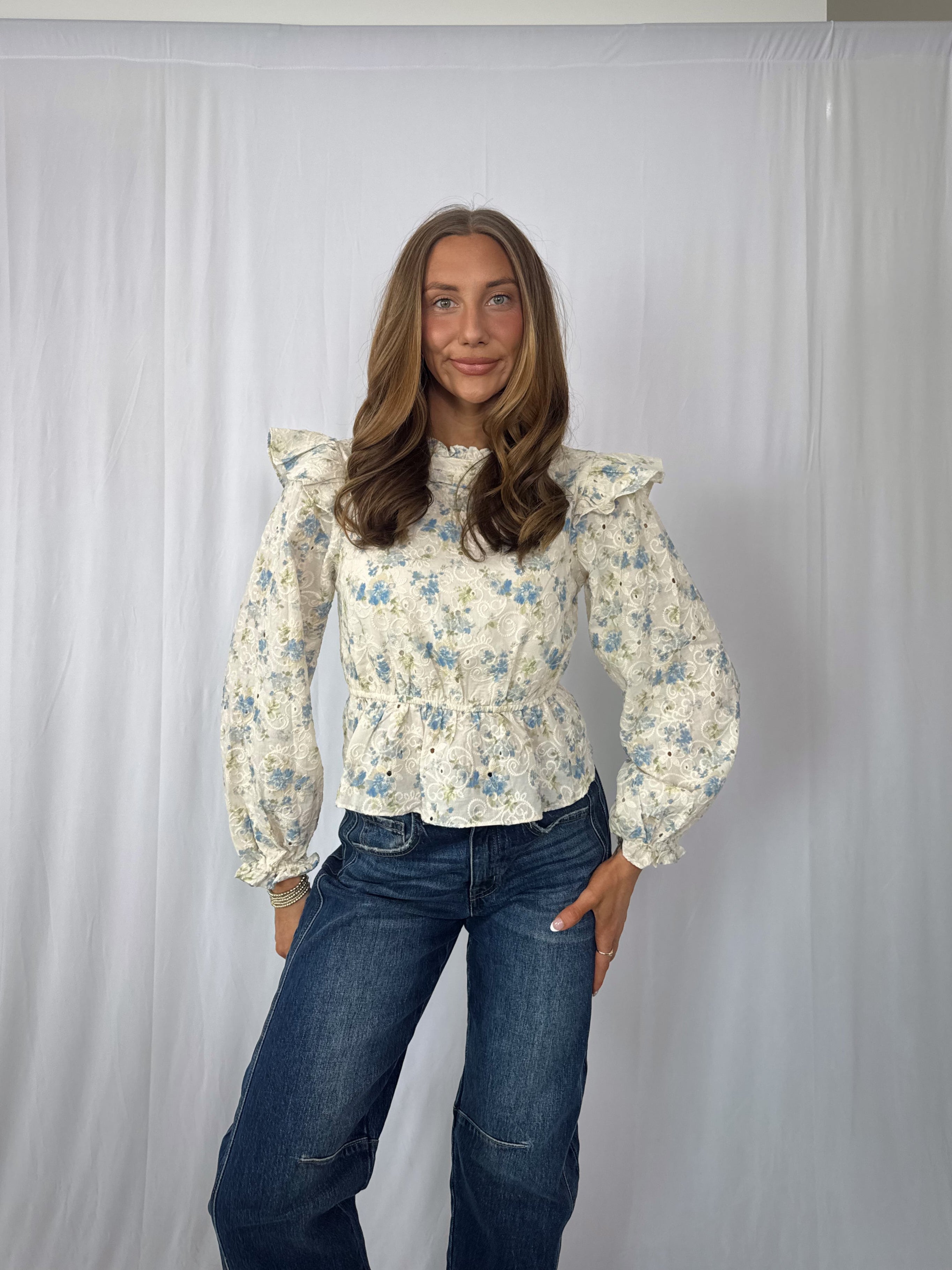 Woman wearing a floral blouse and jeans against a plain background
