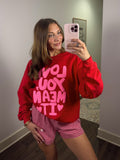 Person wearing a red sweatshirt with pink text and checkered shorts taking a mirror selfie.