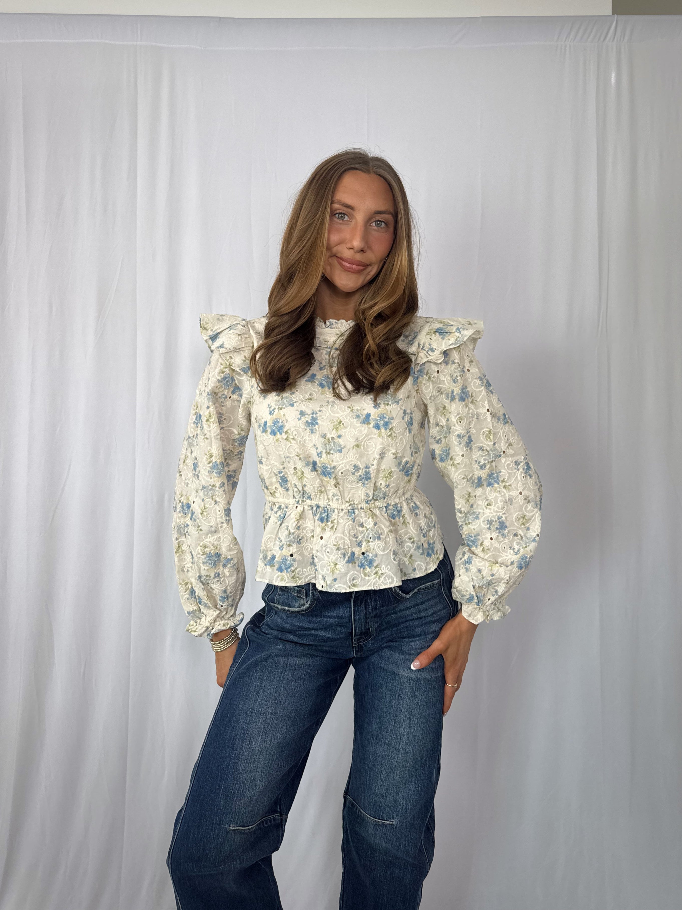 Woman wearing a floral blouse and jeans against a plain background