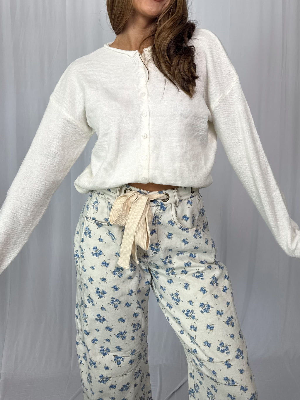 Woman wearing a white cardigan and floral pants against a plain background