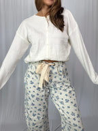 Woman wearing a white cardigan and floral pants against a plain background