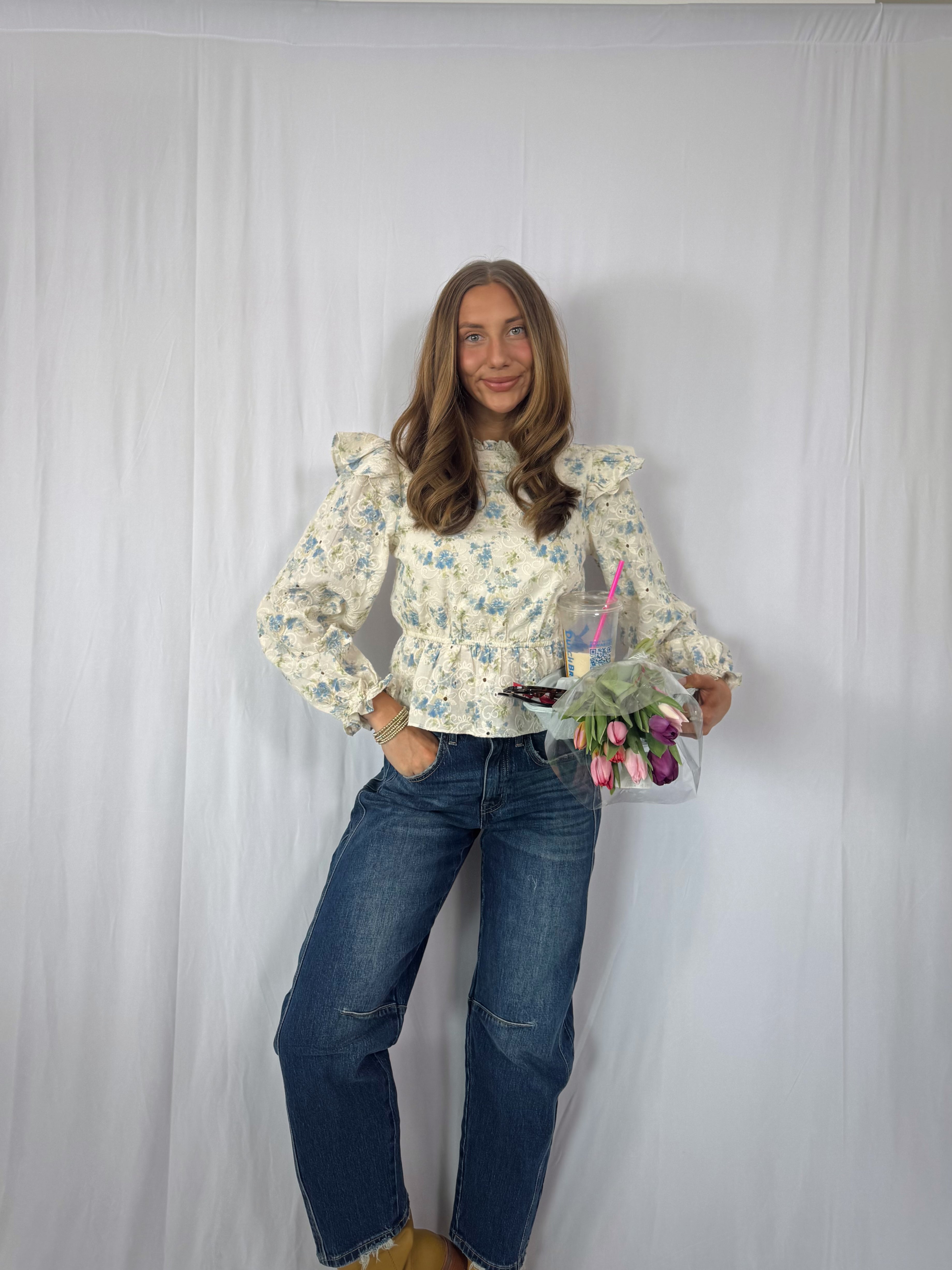 Woman wearing a floral blouse and jeans holding a bouquet of flowers against a white background