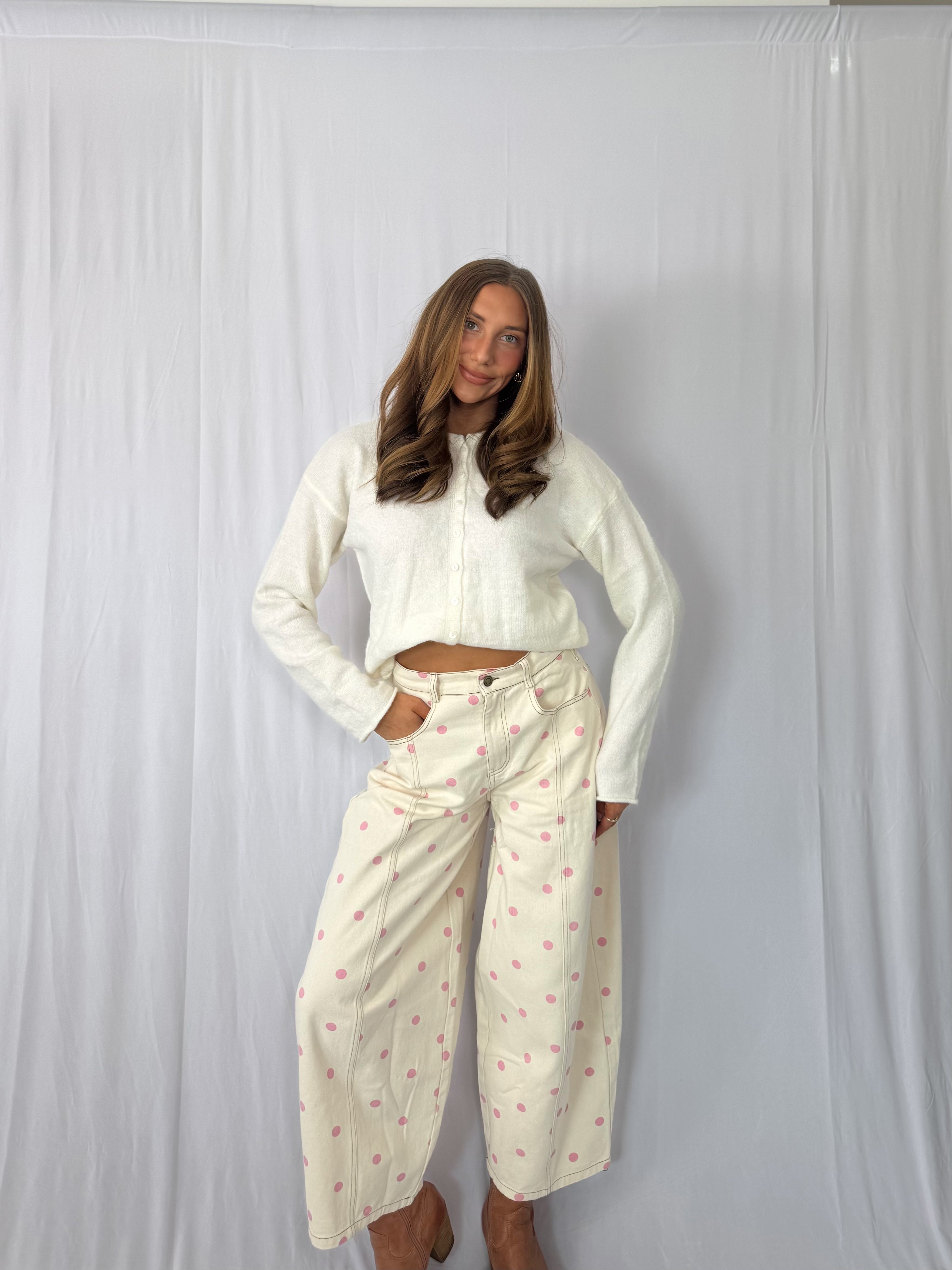 Woman wearing a white long-sleeve top and light-colored pants with a subtle pattern against a plain background