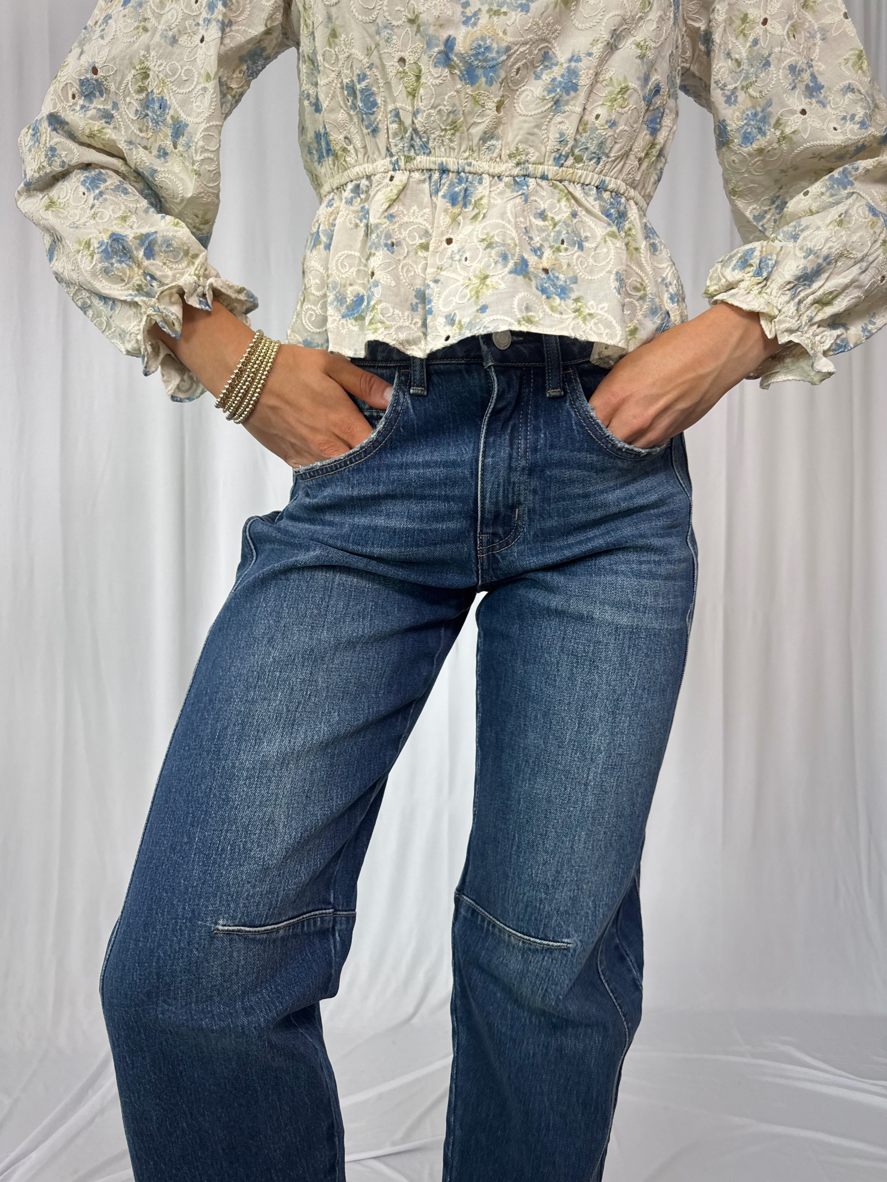 Person wearing a floral blouse and blue jeans against a white background