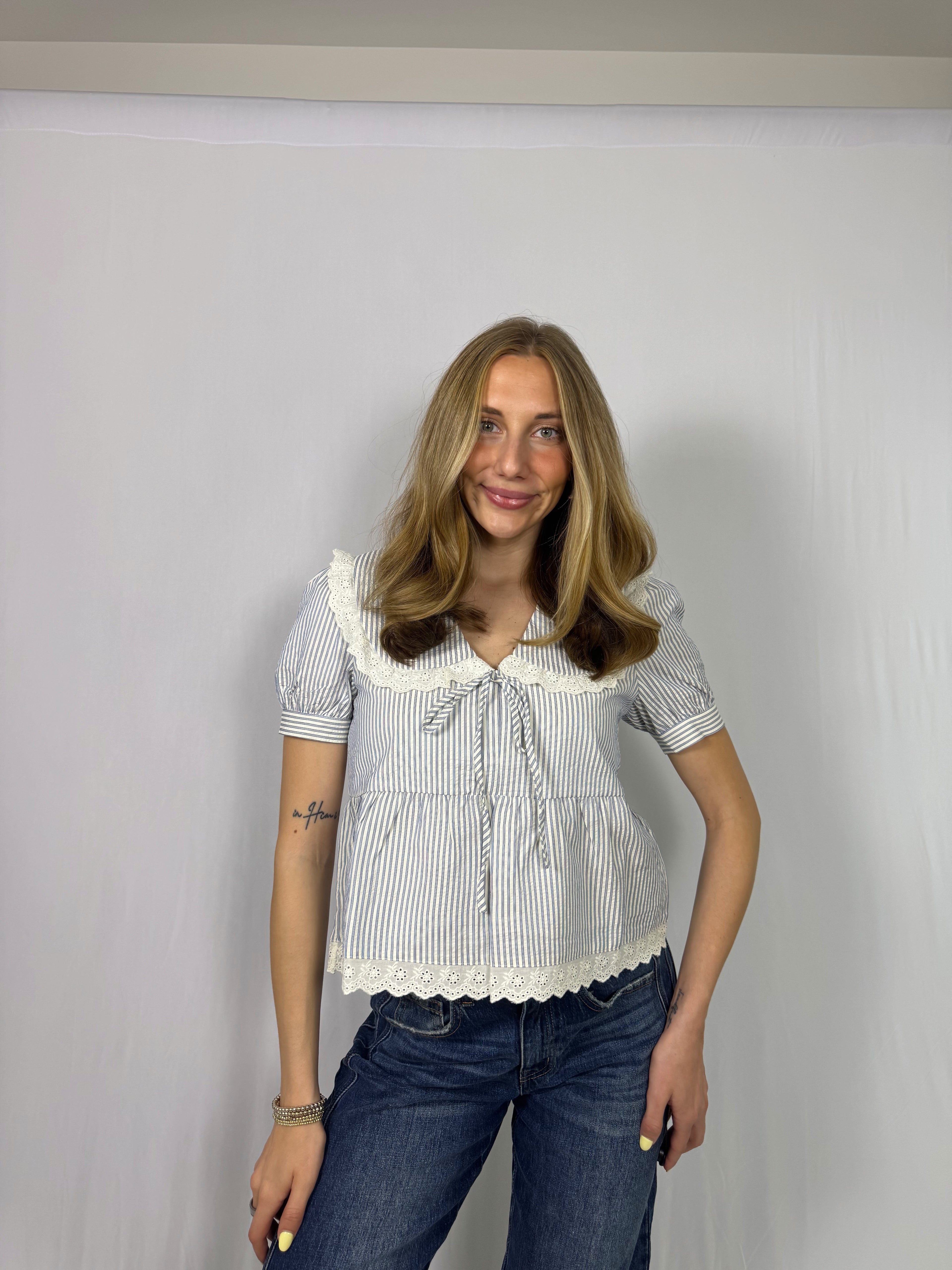 Woman wearing a striped blouse with lace details and blue jeans against a plain background