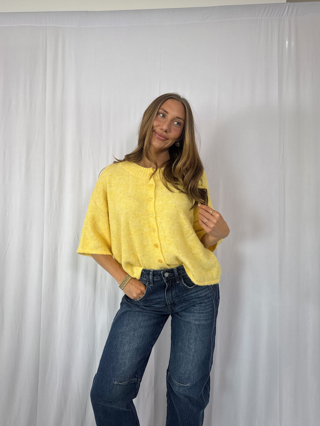 Person wearing a yellow shirt and blue jeans against a white backdrop