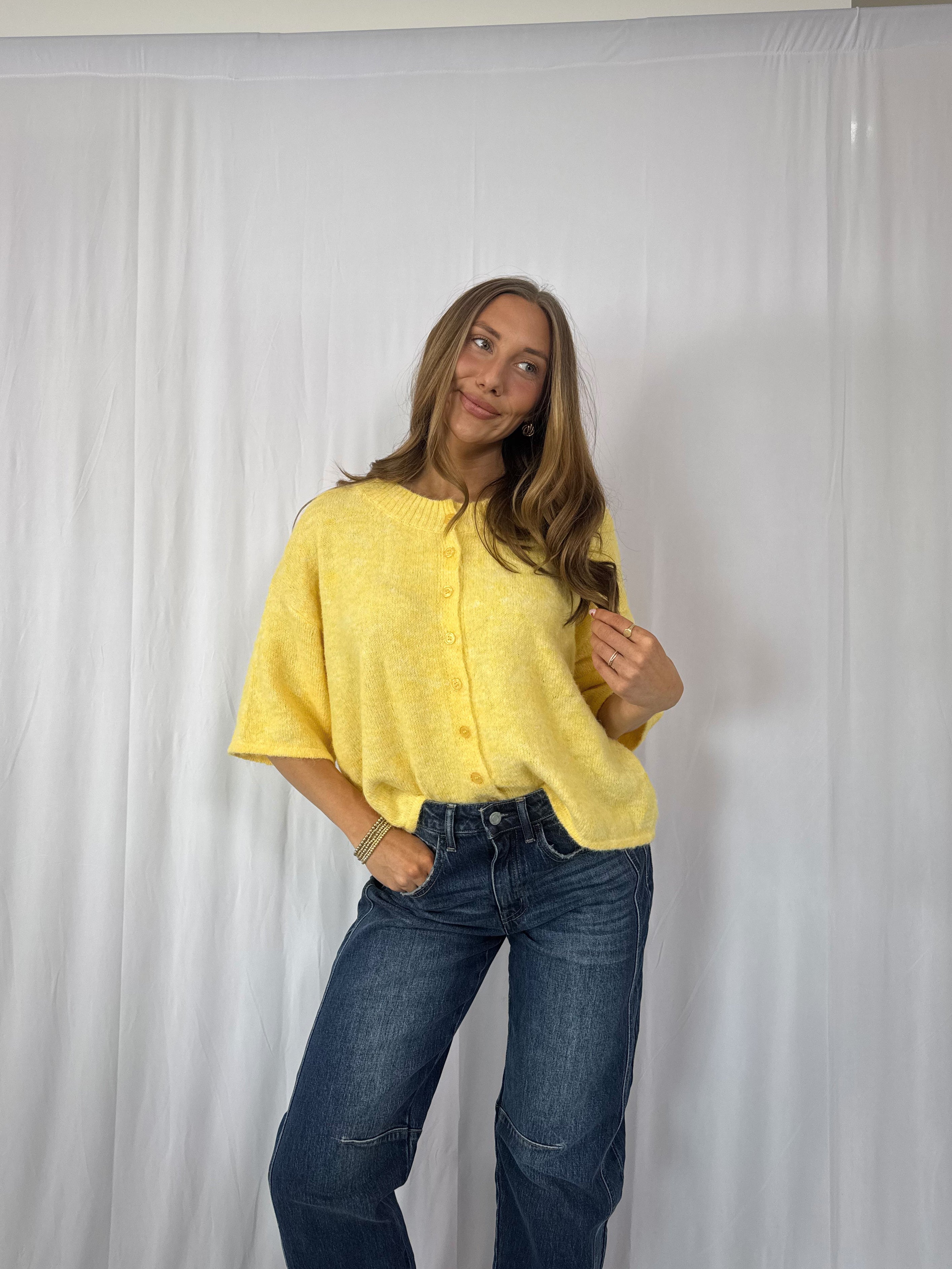 Person wearing a yellow shirt and blue jeans against a white backdrop