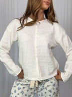 Woman wearing a white button up top with floral pajama pants against a plain background