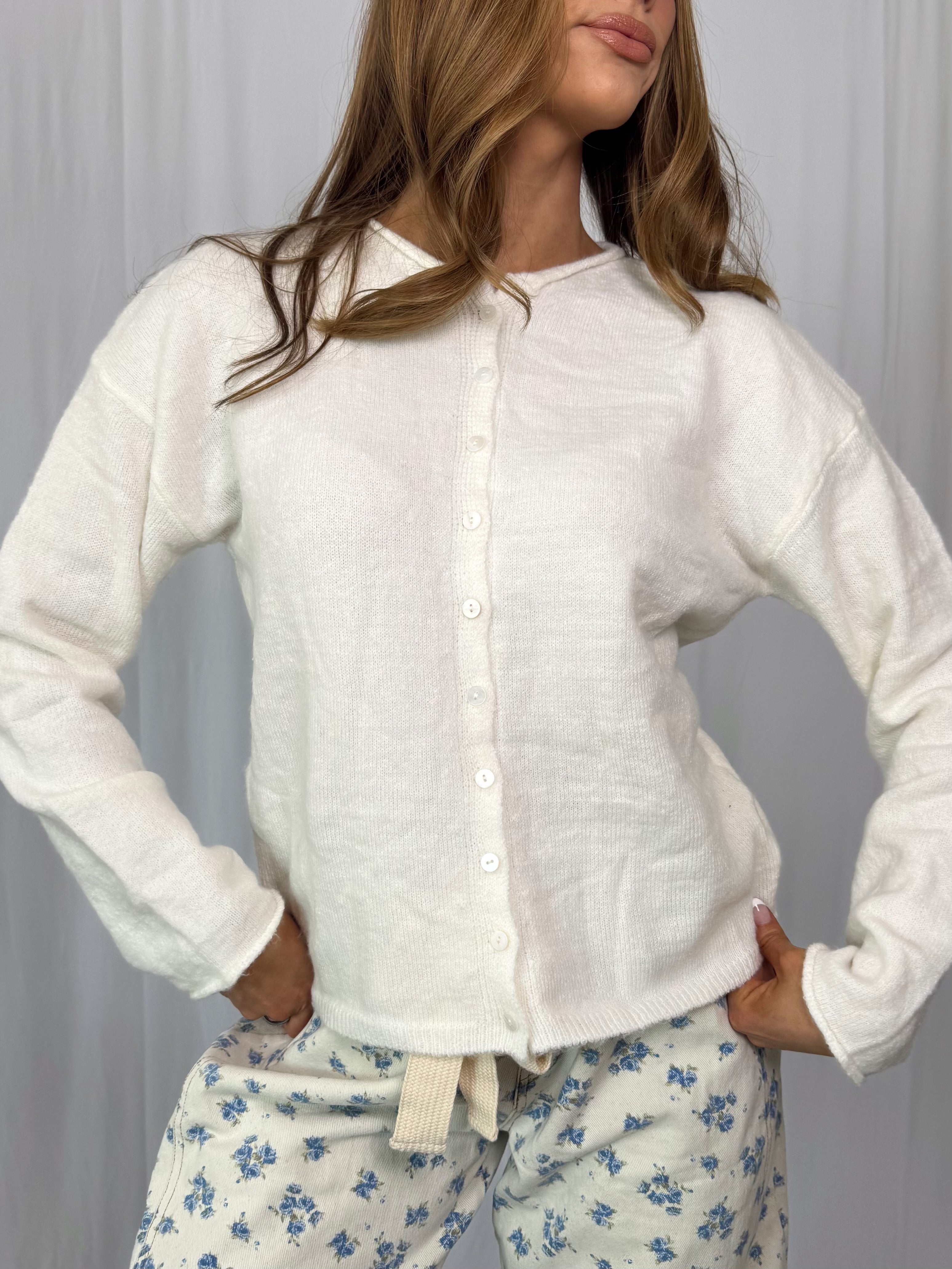Woman wearing a white button up top with floral pajama pants against a plain background