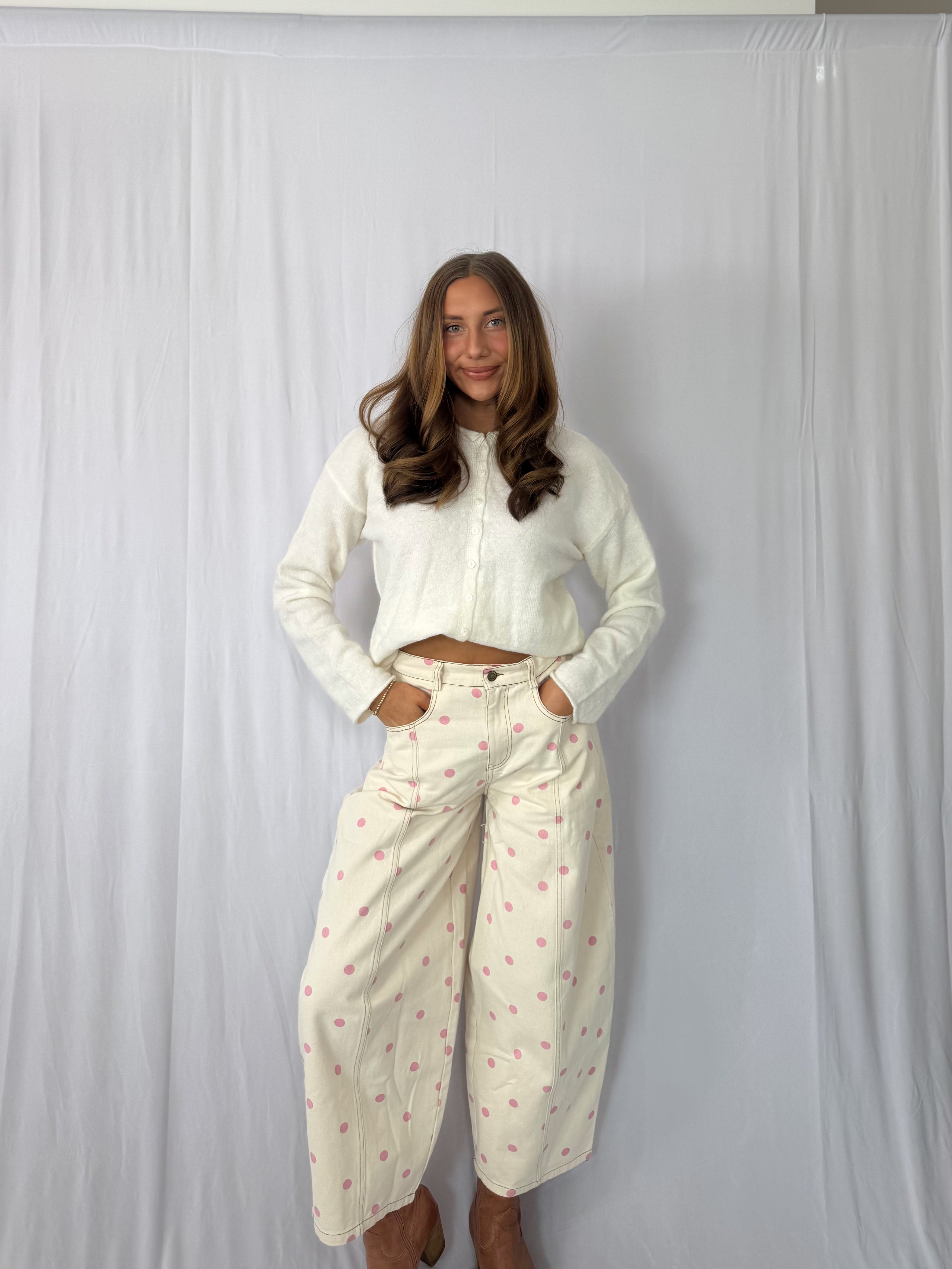 Woman wearing a white sweater and patterned pants against a plain background