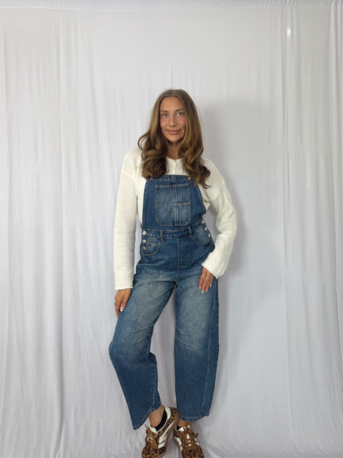 Person wearing blue denim overalls and a white long-sleeve shirt against a white background