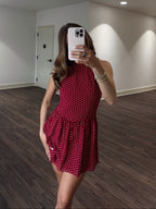 Woman taking a mirror selfie wearing a red polka dot dress in a room with wooden flooring and white walls.