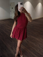 Person wearing a red polka dot dress taking a mirror selfie in an indoor setting.