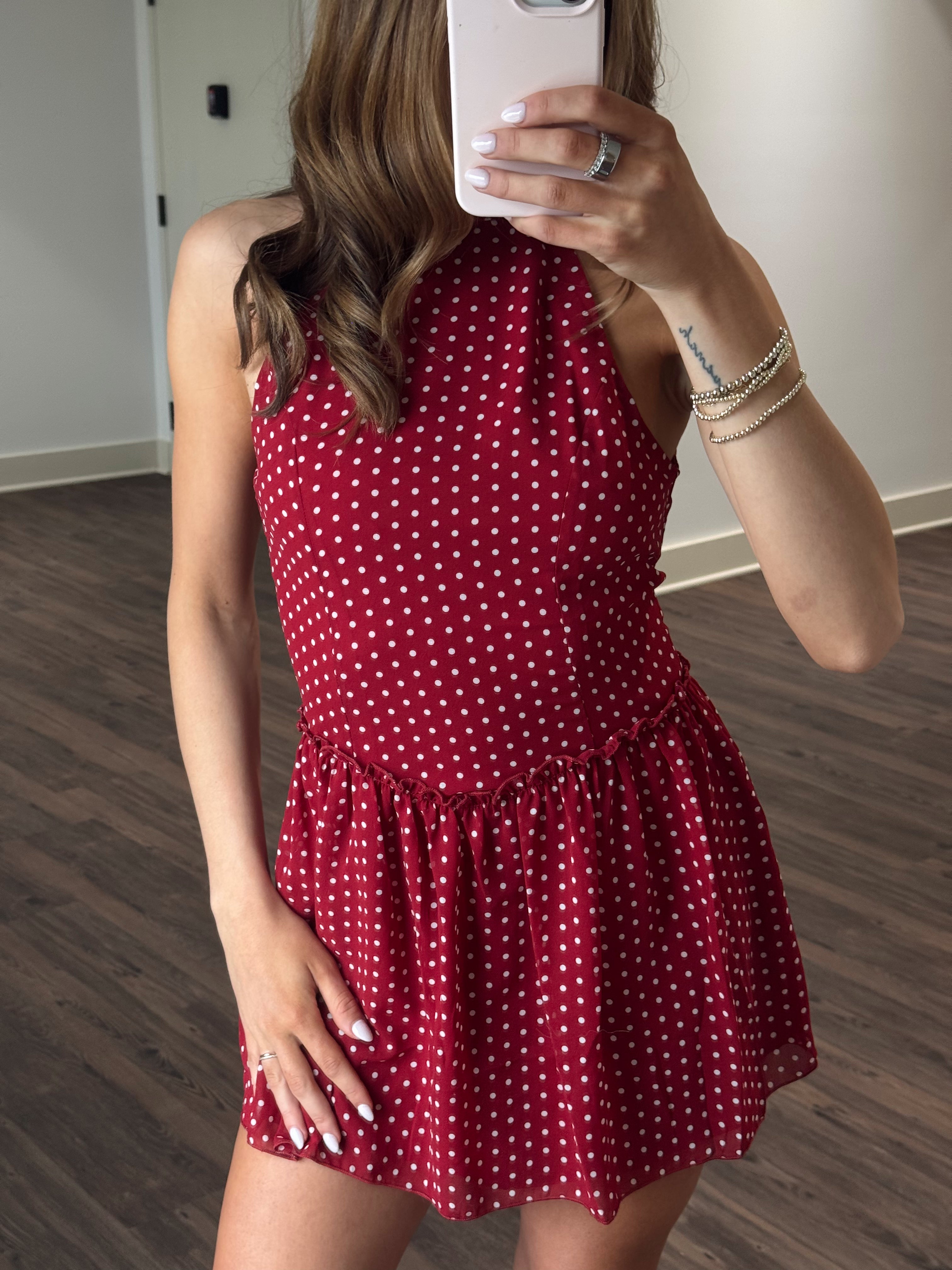 Person wearing a red polka dot dress taking a mirror selfie.