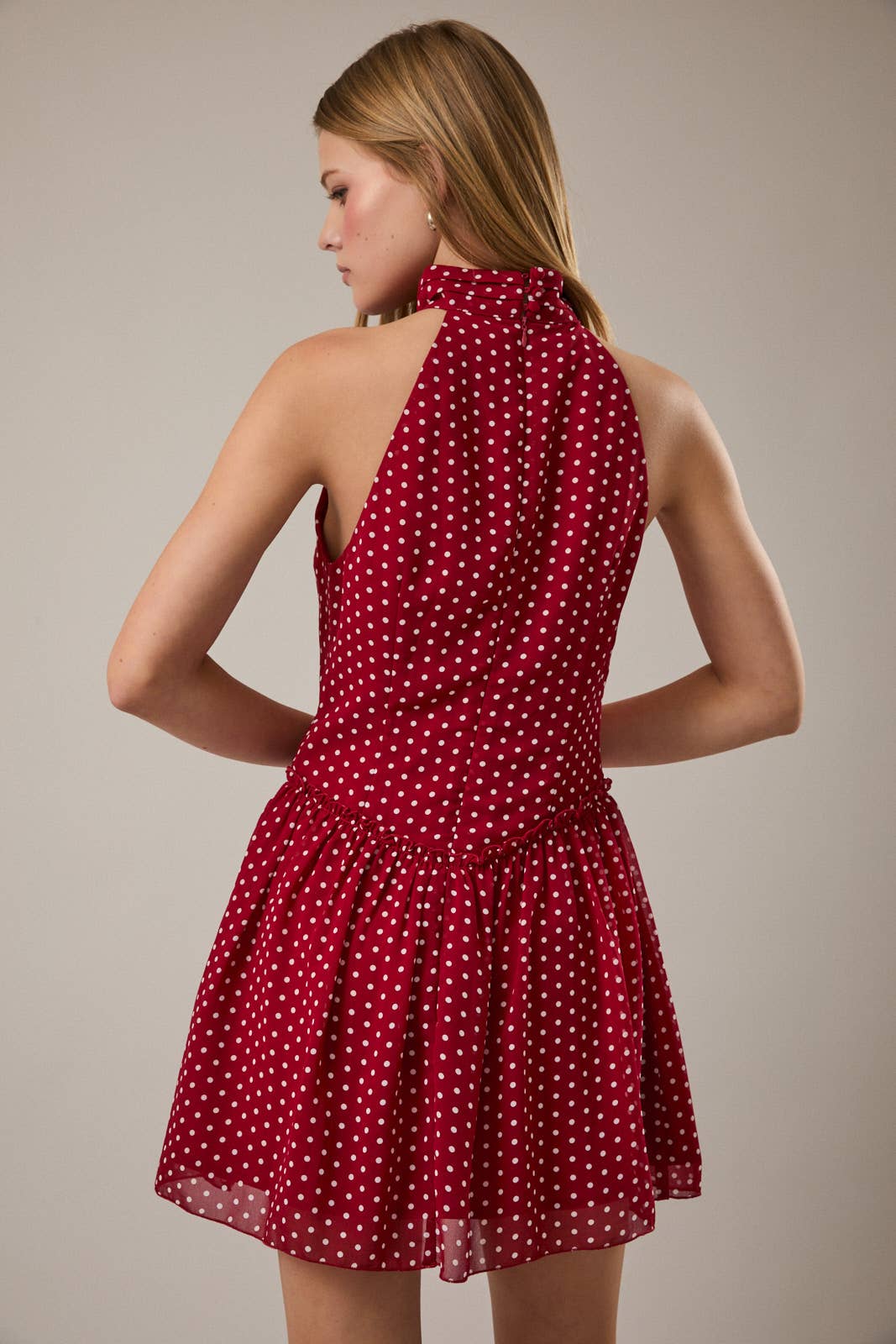 Red polka dot dress worn by a model on a plain background. Model is turned around showing the back of the dress.