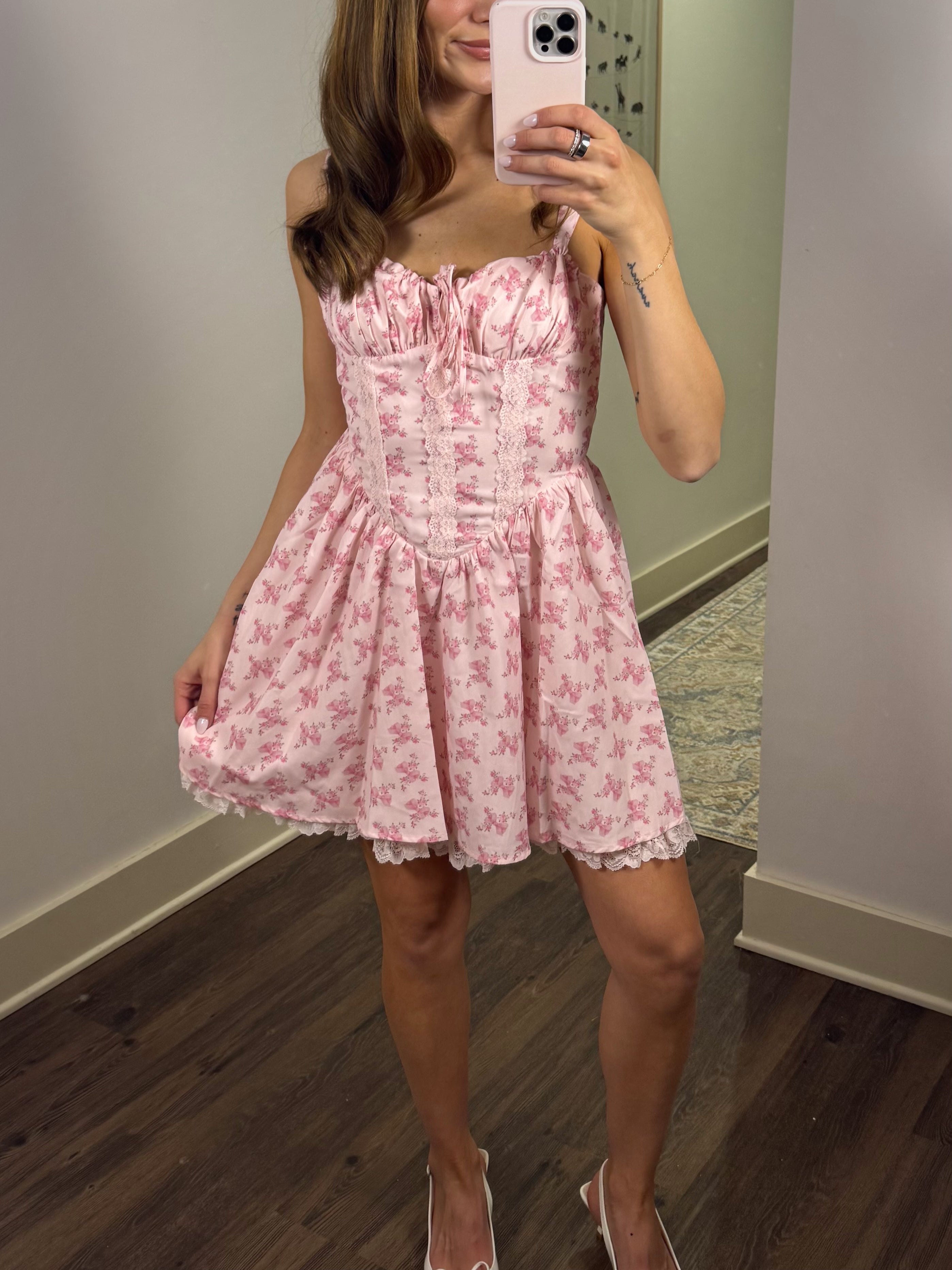 Woman wearing a pink floral dress taking a mirror selfie.