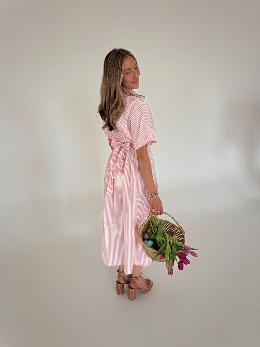 Woman in a pink striped dress holding a basket of flowers against a plain background